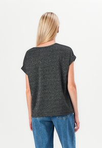 Short-sleeve top in black with glittery texture, relaxed fit, round neckline, and rolled cuffs, paired with blue denim jeans.