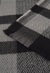 Couverture en laine noire et grise tissée avec un motif à chevrons carreaux et des bords à franges, pliée sur une surface assortie.