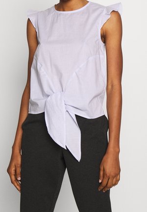 Bezruký světle modrý top s proužky, s volánkovými rameny a předním zavazováním, nošený s černými kalhotami.