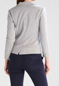 Grijze, lichte blazer met lange mouwen, een geknipt boord, een split aan de achterkant en textuurstof, gecombineerd met navy strakke broek met knoopdetails.