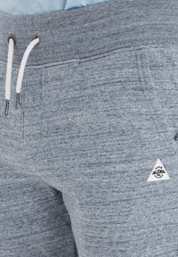 Pantalones de chándal grises con un acabado texturizado, que presentan una cintura con cordón, herrajes plateados y un pequeño acento de logotipo triangular.