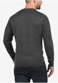 Pull en maille gris foncé avec un col rond et des manches longues, présentant un ourlet et des poignets côtelés, porté avec un jean en denim.