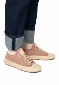 Sneakers in suede rosa chiaro con suole e lacci in gomma crema. Presentano un logo ricamato e cuciture visibili. Jeans scuri a tamburello con fodera azzurro chiaro.