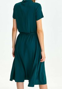 Teppeknädd klänning med cinchad midja, korta ärmar, mjukt tyg och en lätt A-linjeform. Slät textur, minimal design.