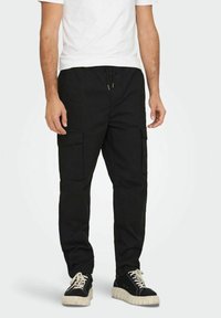 Černé cargo kalhoty s několika bočními kapsami, elastickým pasem a volným střihem. V kombinaci s černými teniskami s bílou silnou podrážkou.