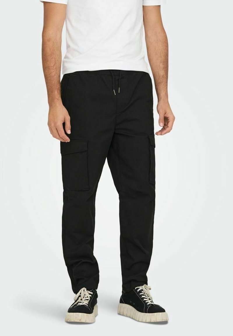 Černé cargo kalhoty s několika bočními kapsami, elastickým pasem a volným střihem. V kombinaci s černými teniskami s bílou silnou podrážkou.