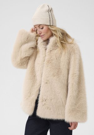 Beige faux fur coat with a wide silhouette, large sleeves, and button closure. Paired with a cream ribbed knit hat with black stripes.