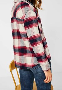 Rood, marineblauw en crèmekleurig geruite flanellen shirt met een kraag, knoop manchet en een relaxte pasvorm, gecombineerd met donkerblauwe jeans.