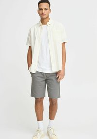 Light-colored button-up shirt with short sleeves over a white T-shirt, paired with gray shorts and cream sneakers. Simple design, casual fit.