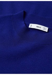 Gros plan d’un pull bleu à col rond avec un col côtelé et une étiquette blanche de la marque MNG cousue à l’intérieur de l’encolure.