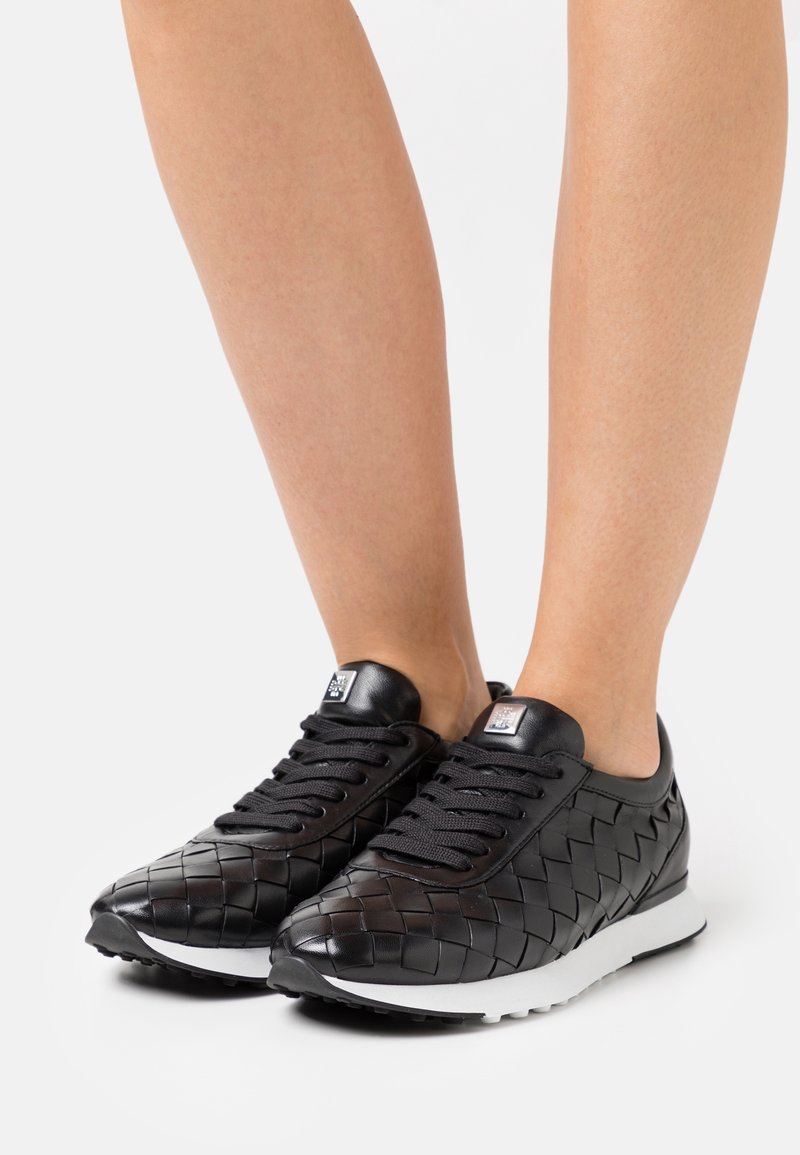 Svarta lädersneakers med vävt mönster, med svarta snören, en vadderad krage och en vit sula för kontrast.