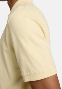 Polo in cotone giallo chiaro con maniche corte e polsini a coste, caratterizzato da una texture liscia e un design classico.