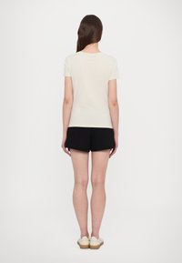 Ljust beige kortärmad t-shirt med rund halsringning, kombinerad med svarta shorts. Observera: slätt tyg utan synliga mönster eller detaljer.