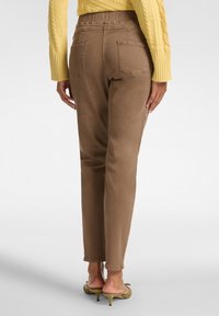 Pantalones marrones de cintura alta con pierna ajustada, bolsillos traseros y un acabado suave. Combinados con un suéter amarillo de punto trenzado.