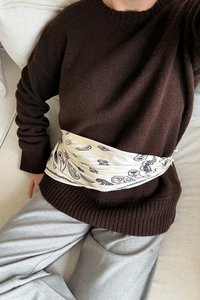 Pull en maille marron foncé avec ourlet côtelé ; ceinture style bandana crème avec motif paisley noir ; pantalon large gris clair.