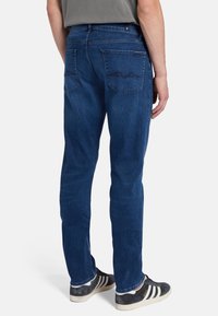 Jeans in denim blu slim-fit con una trama delicata, tasche posteriori con cuciture curve e vita intermedia. Indossati con sneaker scure.
