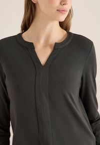 Musta pitkähihaisen paita, jossa on v-kaula-aukko ja pyöreä kaulus, sileä pinta ja pystysuuntaiset sauma-yksityiskohdat.