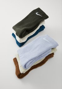 Assorted crew socks in ribbed design. Colors: dark green, blue, cream, light blue, beige, and brown. Nike logo on dark green sock.