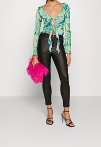 Kwiatowa zielona bluzka z długim rękawem i wiązaniami w talii, zestawiona z czarnymi, obcisłymi skórzanymi spodniami oraz jaskrawo różową torebką z futra sztucznego. Czarne sandały na obcasie.