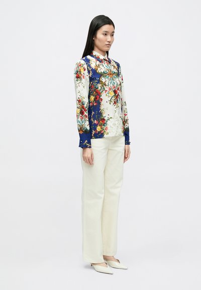 Košeľa s dlhým rukávom s kvetinovým vzorom v červenej a zelenej farbe na bielom pozadí, s námornícky modrým golierom. Kombinovaná s krémovými nohavicami.