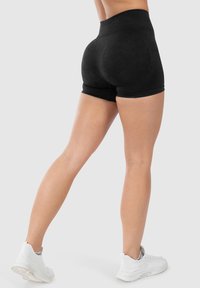 Hoge zwarte shorts van zachte stof, met een aansluitend ontwerp. Strak affittende zoom met een gladde textuur. Draagt met witte sportschoenen.