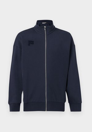 Marineblå jakke med glidelås, stående krage, lange ermer, ribbestrikkede mansjetter og nederkant, og subtil teksturert logo på venstre bryst.