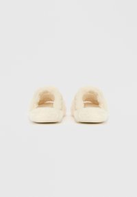 Fur-voering, open rug-slippers in een zachte crème kleur met een pluche textuur en een vlakke zool, ontworpen voor comfort en ontspanning.