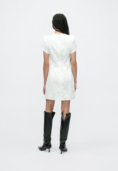 Bela teksturirana obleka s kratkimi napihnjenimi rokavi, prilegajočim pasom in razširjeno krilom, kombinirana s črnimi škornji do kolen s koničastim prstom.