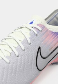 Bijela sportska cipela s teksturiranim gornjim dijelom, s gradijentnim uzorkom u ružičastoj i ljubičastoj boji. Crni Nike logo i bijele vezice.