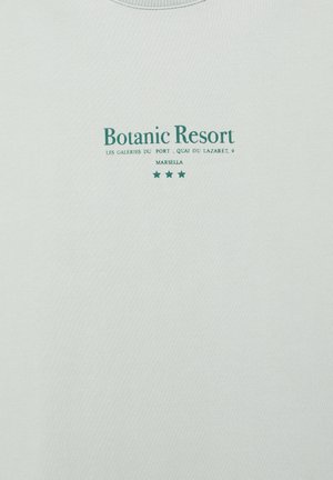 Text Botanic Resort s adresou "Les Galeries du Port, Quai du Lazaret, 9 Marsella" a tromi zelenými hviezdami potlačenými na svetlej látke.