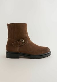 Stivale alla caviglia in suede marrone con suola nera bassa a tasselli e cinturino laterale con fibbia, dotato di zip posteriore e pannello elastico.