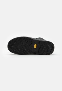 Schwarze Gummisohle mit strukturiertem Oberfläche, ausgestattet mit Zickzack-Profil und einem gelben Logoakzent. Geeignet für Outdoor-Aktivitäten.