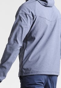 Gray hooded jacket with a smooth texture, featuring a straight cut and seam detailing on the back. Worn over navy pants.