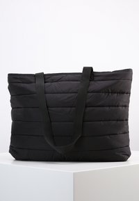 Sac cabas matelassé noir avec deux anses en tissu, doté d'une texture matelassée et d'une forme rectangulaire. Extérieur doux sans aucune quincaillerie visible.