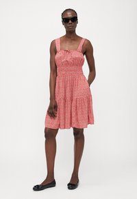 Vestido rojo floral con cuerpo fruncido y tirantes anchos, falda fluida, llevado con bailarinas negras y gafas de sol, tejido texturizado, diseño casual.