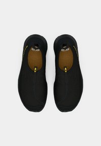 Black slip-on shoes made of fabric with textured surface. Features elastic openings, cushioned insoles, and rubber outsoles. Yellow accents visible.