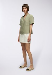 Camicia a maniche corte di un verde chiaro con trama, gonna in denim bianco e espadrillas intrecciate con punte nere. Design semplice e pulito.