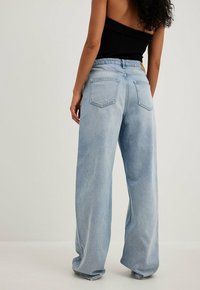 Jean large bleu clair en denim, avec taille haute, cinq poches et une texture légèrement délavée. Vue de dos affichée.