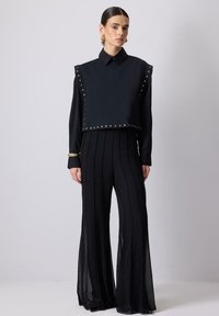 Sort to-delt outfit med en cropped top med nitter og bukser med vidde, der har lodrette striber, lavet af let flydende stof.