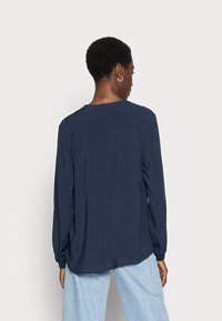 Blusa de mangas longas azul-marinho com decote redondo, textura suave, detalhe de yoke nas costas e ajuste relaxado, combinada com jeans azul claro.