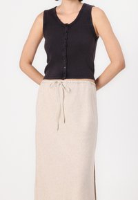 Svart ribbad ärmlös topp med knäppning, kombinerad med en beige maxikjol med dragsko som har en sidoflog och subtil textur.