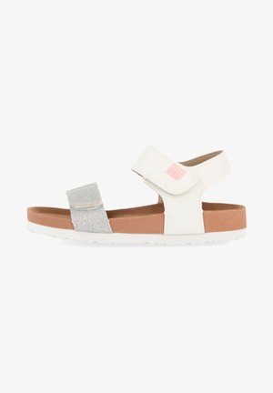 Sandalia blanca y plateada para niños con correas ajustables y una plantilla acolchada marrón, mostrada de perfil sobre un fondo blanco.