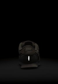 Zapatilla negra de Nike con una parte superior texturizada, una franja reflectante en el talón y una suela lisa. El diseño es minimalista y aerodinámico.