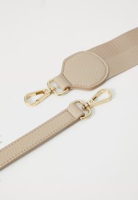 Bracelet en cuir beige avec une texture lisse; présente un clip et des accessoires dorés; comprend une section en tissu texturé et plus large.