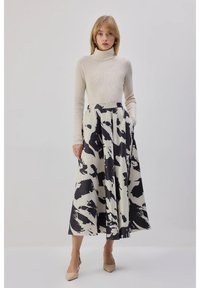 Beige geribbelde coltrui gecombineerd met een lange, zwart-wit abstracte patroon rok, met een brede tailleband en zijzakken.