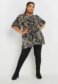 Tunic a fantasia nera e beige con maniche corte e ampie e scollatura a V, abbinata a leggings neri e stivali neri alla caviglia.