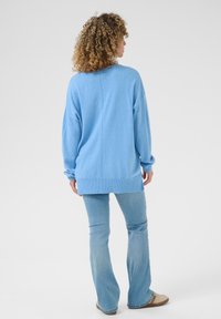 Světle modrý oversized svetr s kleslými rameny, žebrovanými manžetami a detailem švu na přední straně, spárovaný se světle modrými rozšířenými džínami.