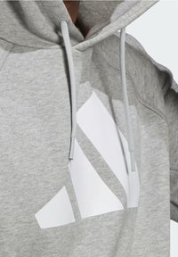 Sudadera gris con un gran logo geométrico blanco. Material suave con capucha ajustable y textura acanalada en los puños.