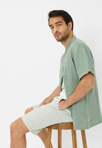 Groene linnen overhemd met korte mouwen en een borstzak, gecombineerd met lichtgestreepte shorts. Beide kledingstukken hebben een ontspannen pasvorm.