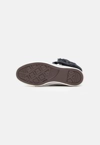 Suela de un zapato negro sin cordones con agarre de goma texturizada, que presenta un borde blanco y una parte superior de tela suave con una textura delicada.
